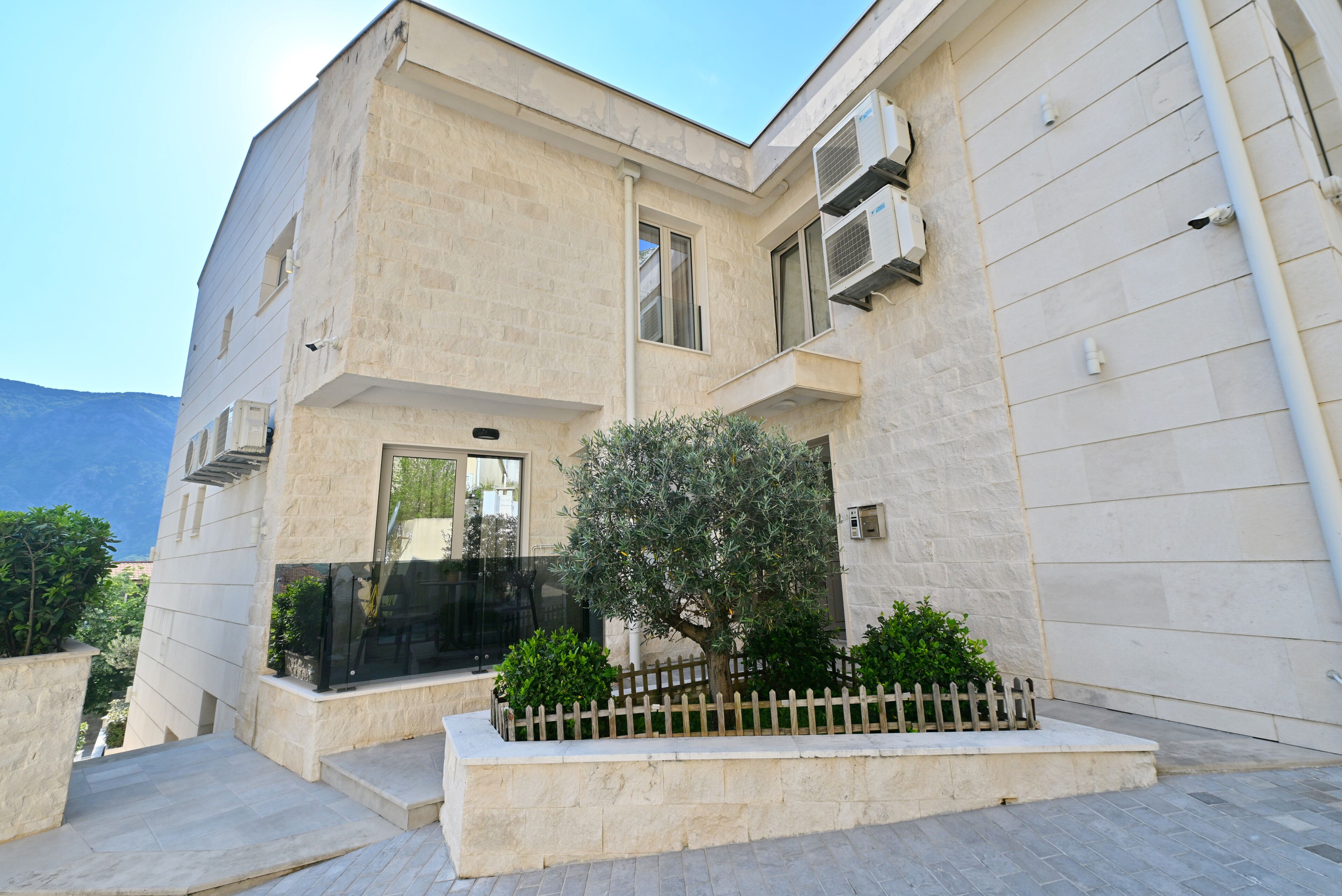 A modern building with a stone facade, a small tree, and a wooden fence.