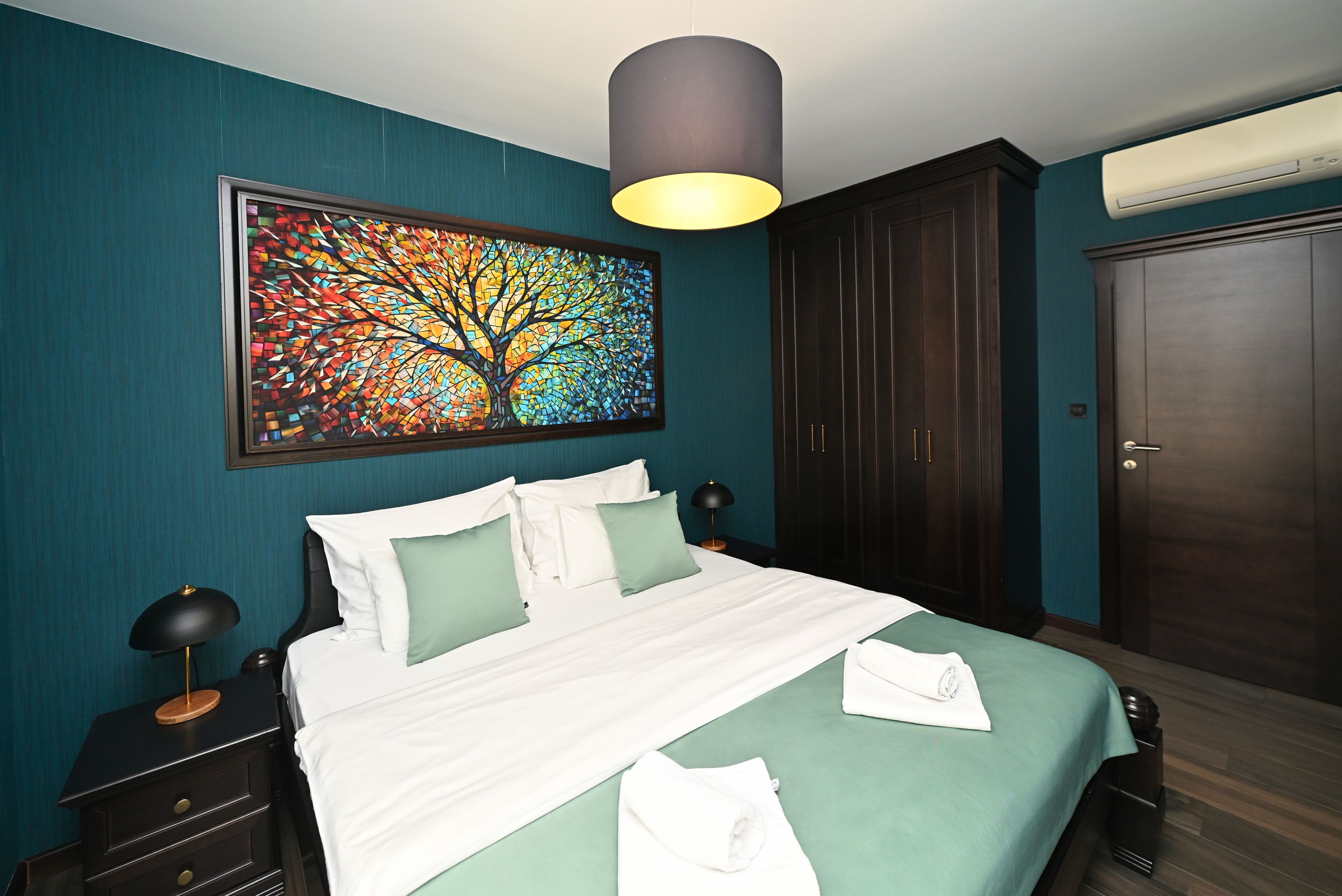 A hotel room with a bed, a nightstand, a lamp, a painting, and a wardrobe.