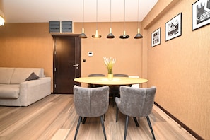 Un comedor moderno con una mesa redonda, sillas grises, un jarrón con flores blancas, luces colgantes y cuadros en la pared.