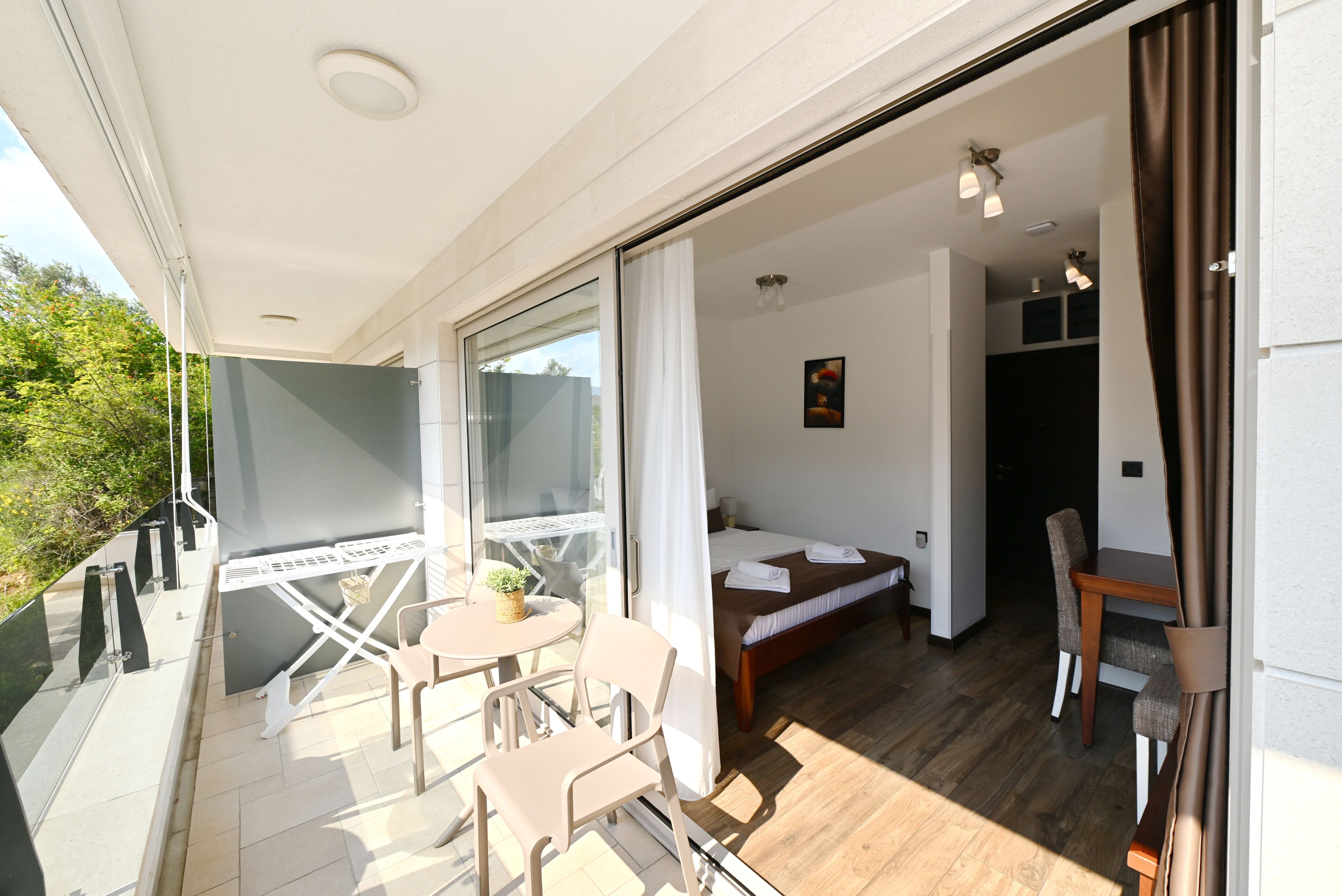 Una habitación con cama, una mesa y una silla, un balcón con mesa y sillas, y vistas a zonas verdes.