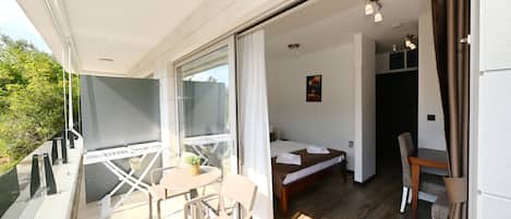 Una habitación con cama, una mesa y una silla, un balcón con mesa y sillas, y vistas a zonas verdes.