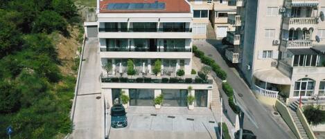 A multi-story building with a flat roof, large windows, and a parking area with cars.