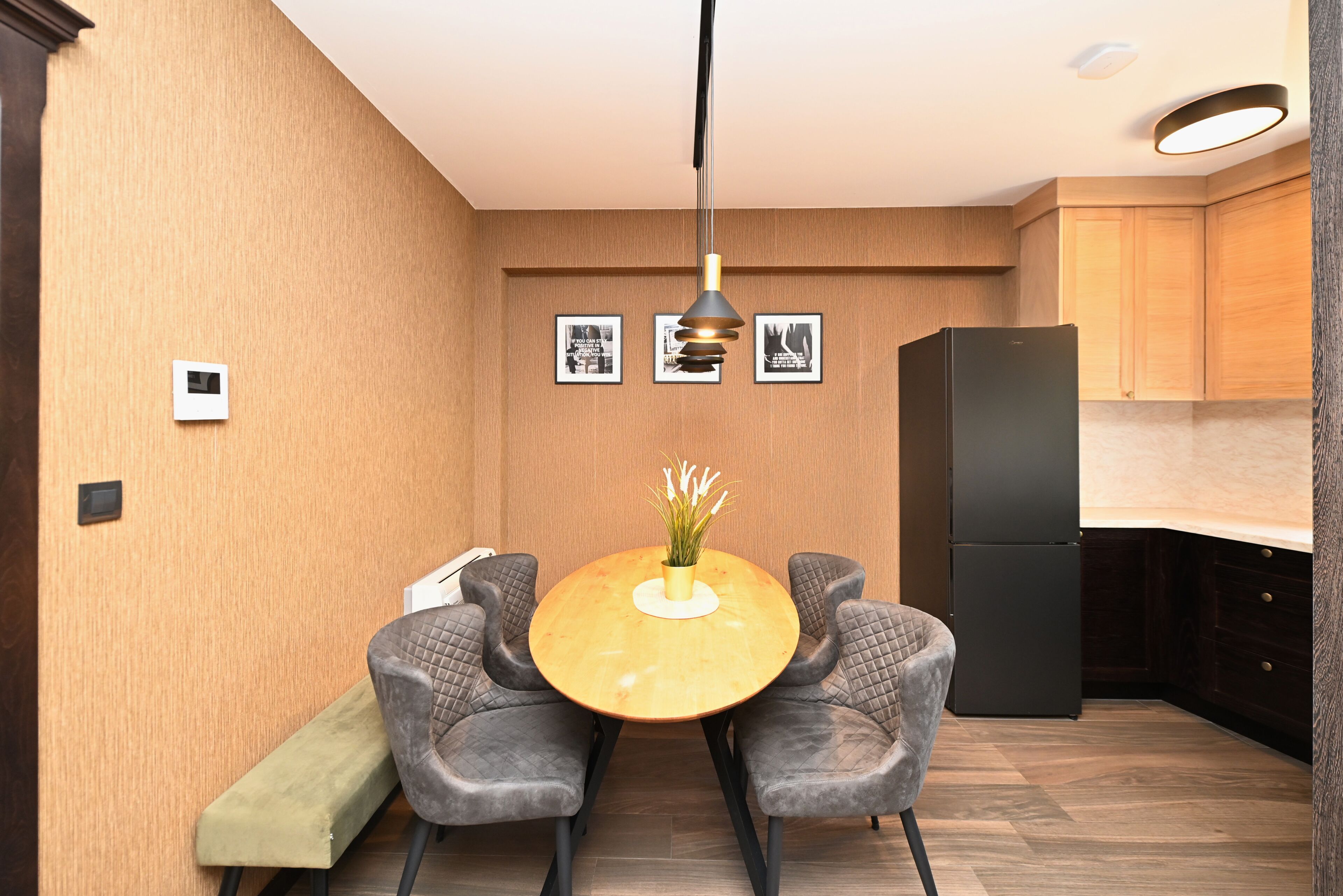 Une cuisine compacte avec un coin repas, des meubles en bois, un réfrigérateur noir et un luminaire suspendu.