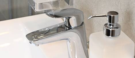 A bathroom sink with a chrome faucet, a soap dispenser, and a clear glass soap container.
