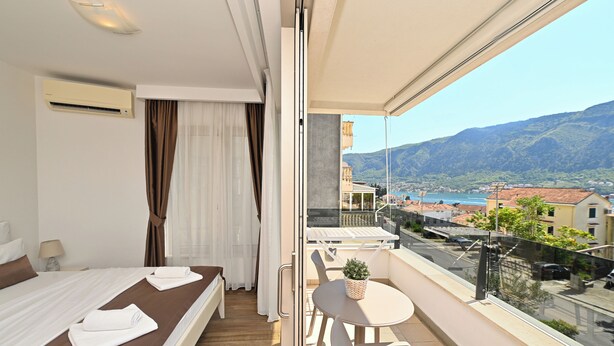 A balcony with a table and chairs, a bed with a view, and a cityscape in the background. - Casa Nuova (Kotor)