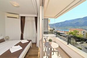 Un balcón con mesa y sillas, una cama con vistas y un paisaje urbano al fondo.