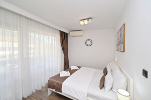 Hotellihuone, jossa on sänky, yöpöytä, seinäkello ja ilmastointilaite.