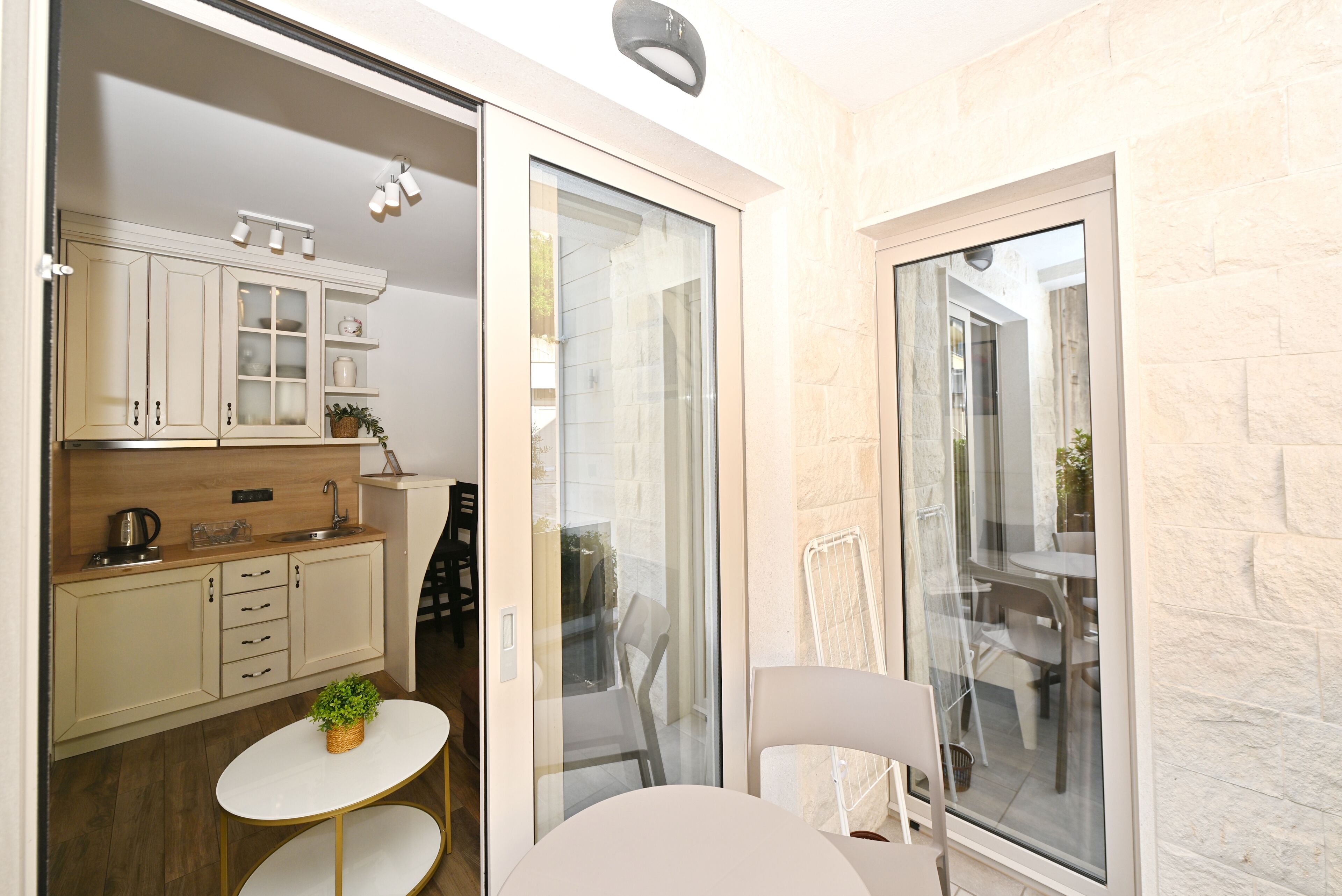 A modern kitchen with white cabinets, a small table, and a potted plant.