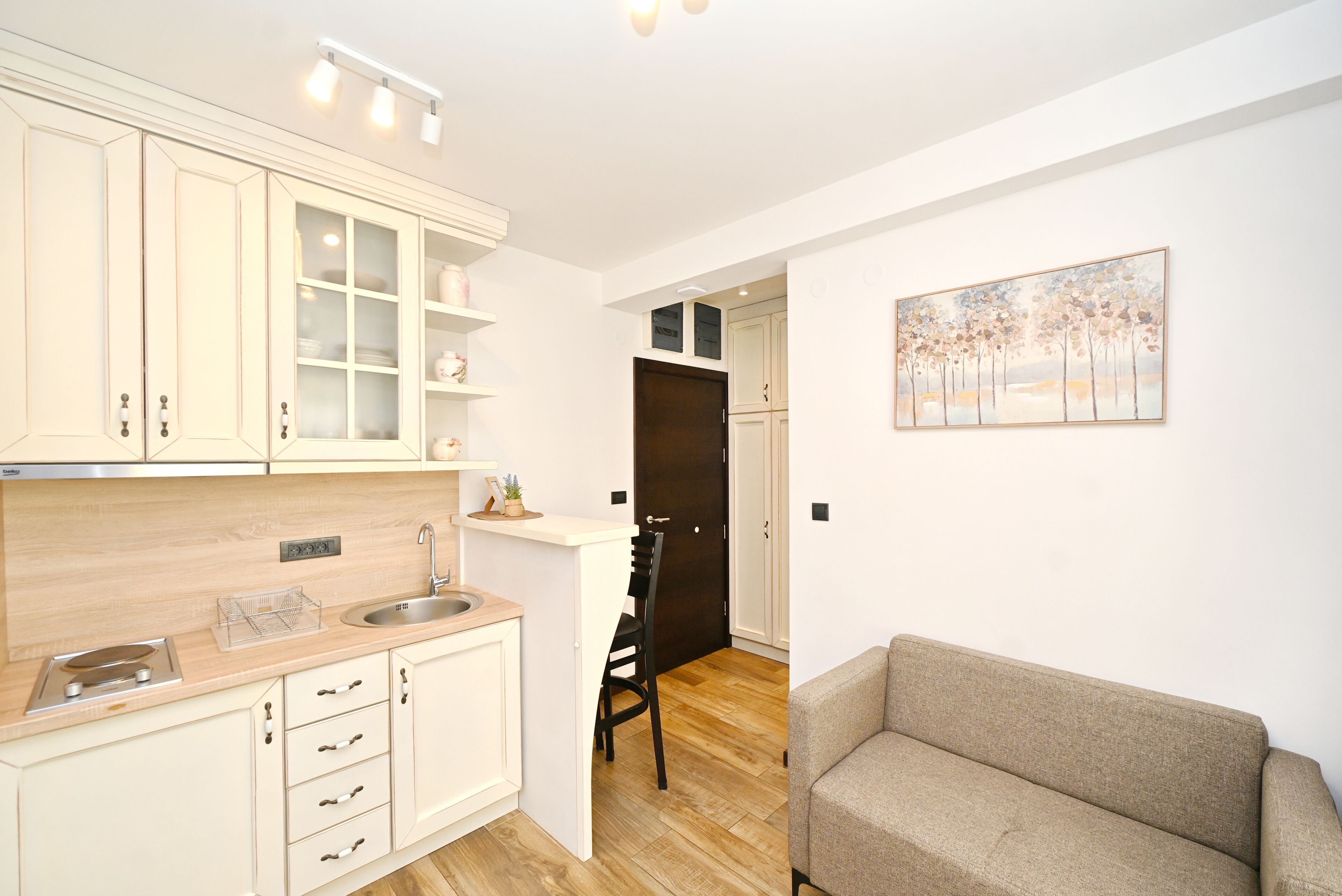 A modern kitchen with white cabinets, a wooden countertop, and a dining area with a sofa.