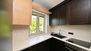 A modern kitchen with dark cabinets, a window, a sink, and a built-in oven. - Casa Nuova (Kotor)