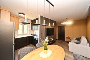 A modern kitchen with a built-in oven, a dining table with a vase of flowers, and a living area with a sofa and a TV.