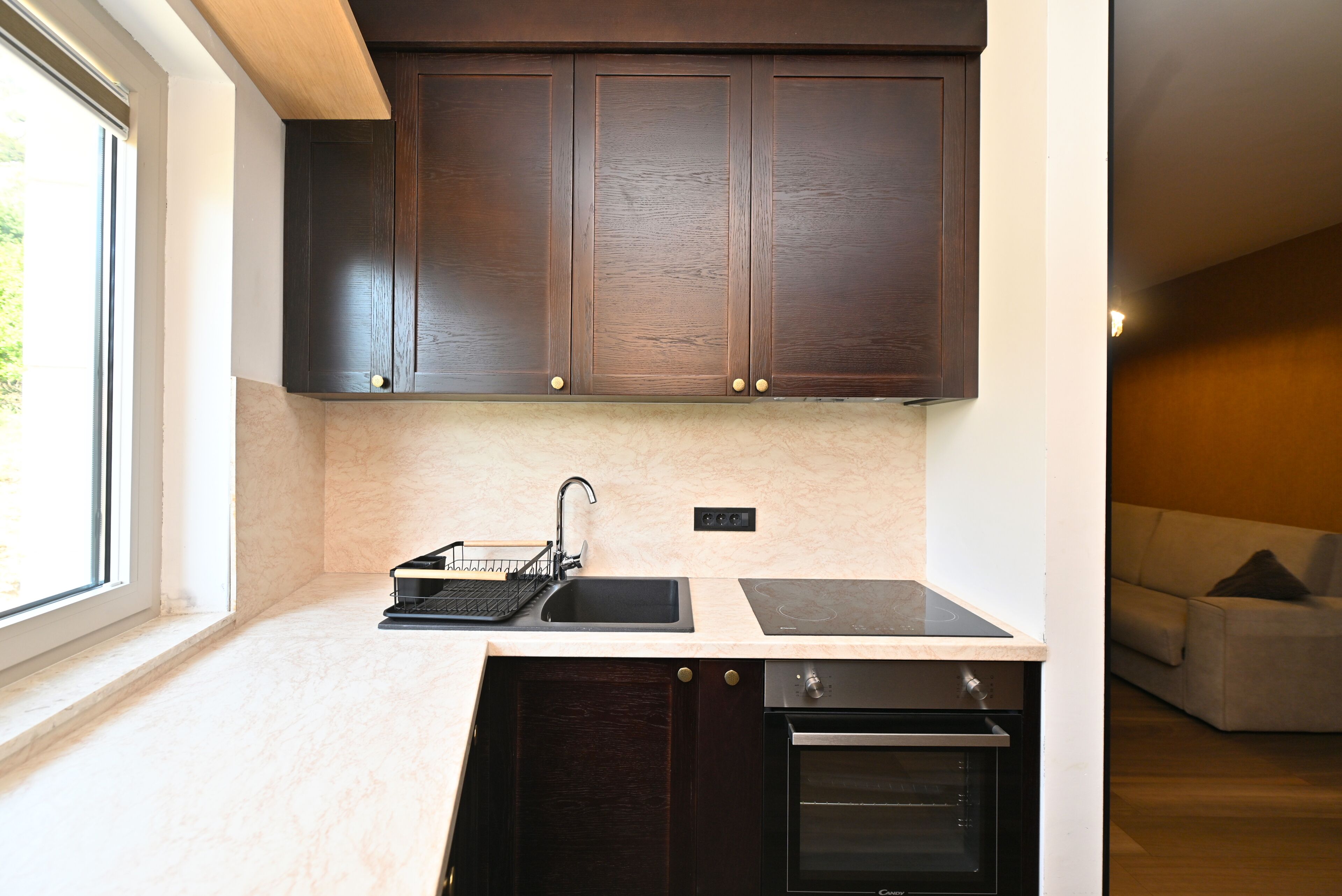 A kitchen with dark wooden cabinets, a built-in oven, and a window providing natural light.