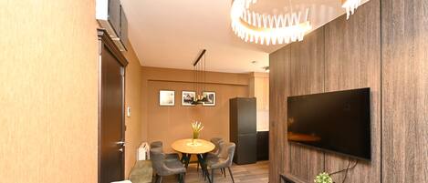 Una sala moderna con televisor de pantalla plana, suelo de madera, una mesa de comedor redonda y un candelabro.
