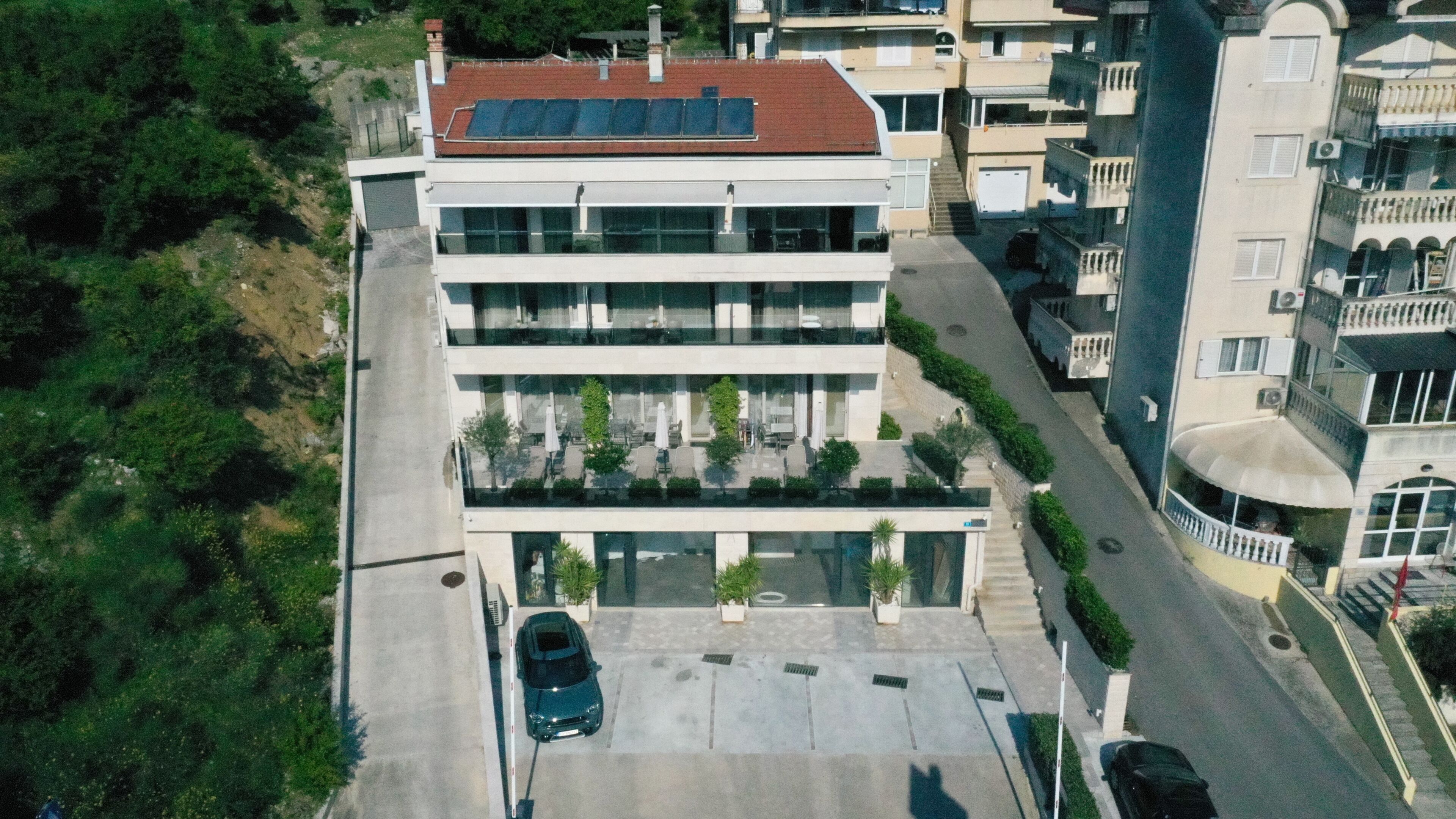 A modern building with a flat roof, large windows, and a parking area with a car.
