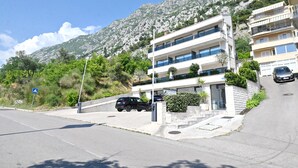 A multi-story building with balconies, a parking area, and a mountainous backdrop. - Casa Nuova (Kotor)