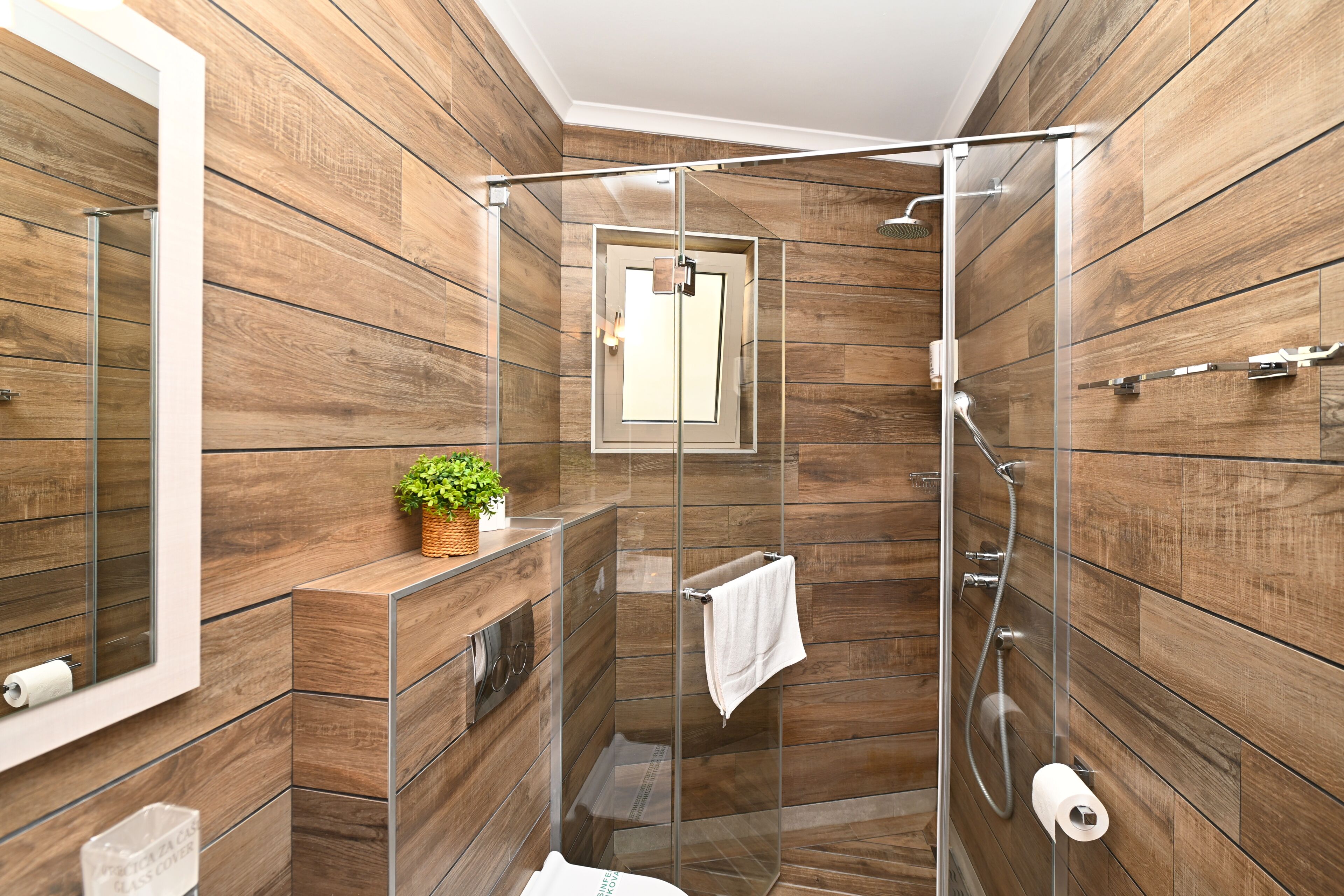 Une salle de bain moderne avec un lambris en bois, une cabine de douche en verre, un miroir et une petite plante posée sur le meuble-lavabo.