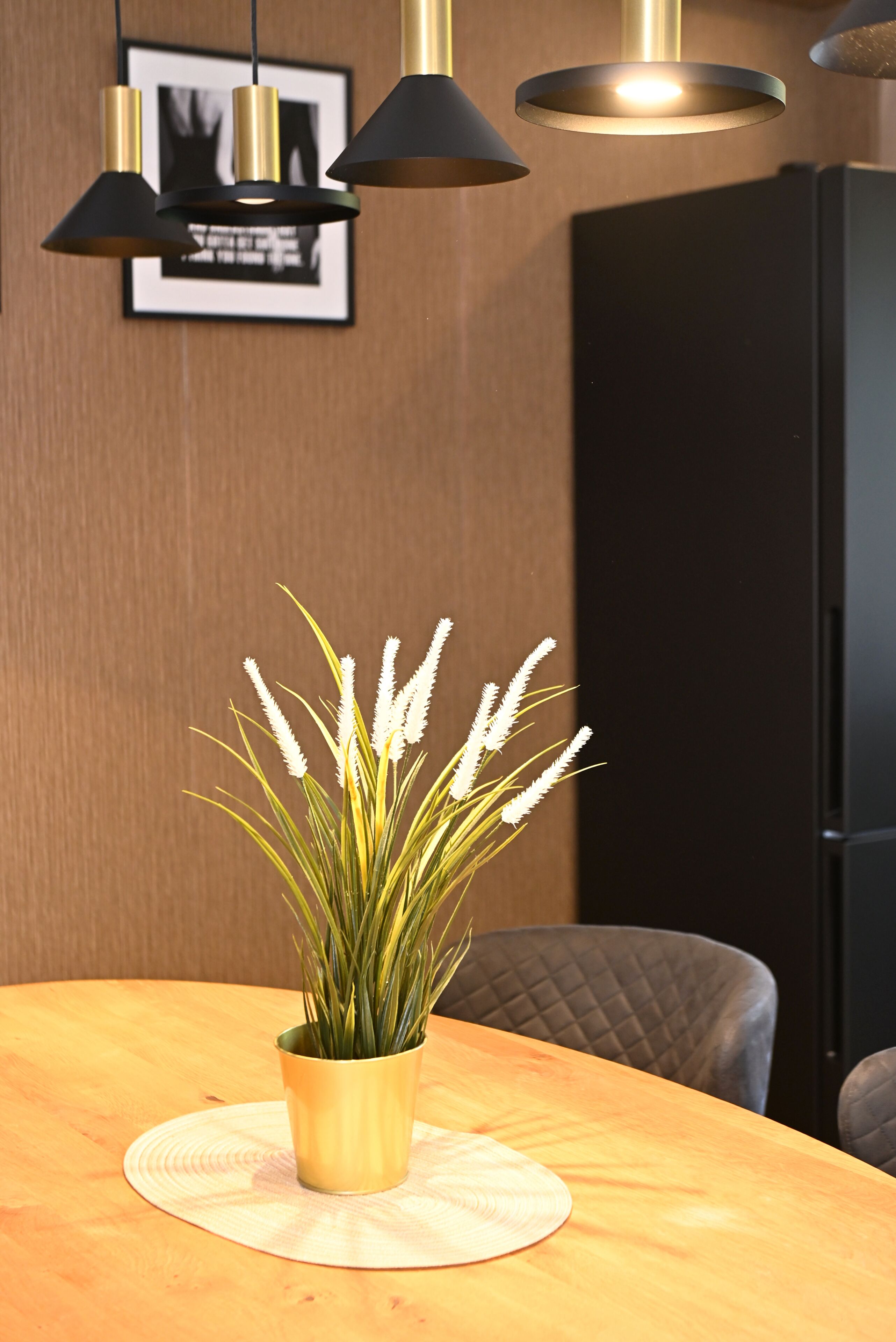 A dining table with a potted plant, a framed picture on the wall, and a black cabinet.