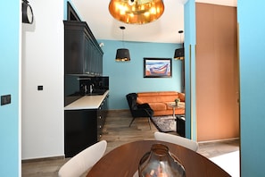A modern kitchen with black cabinets, a dining table with chairs, a sofa, and a painting on the wall.