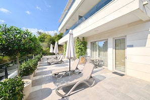 A modern outdoor lounge area with sun loungers, umbrellas, and planters.
