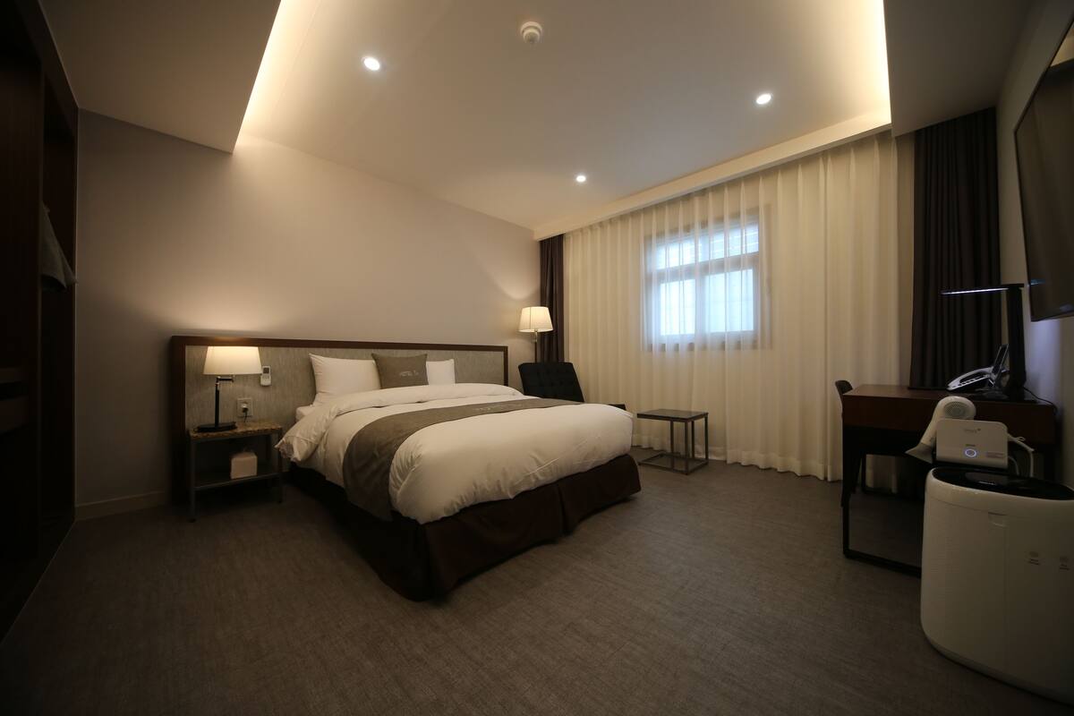 A modern hotel room with a large bed, bedside tables, a desk, and a chair.