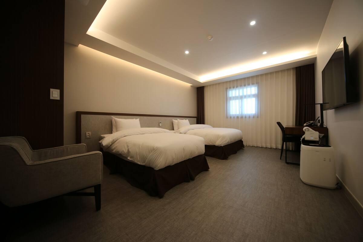 A hotel room with two beds, a sofa, a TV, and a desk with a lamp.