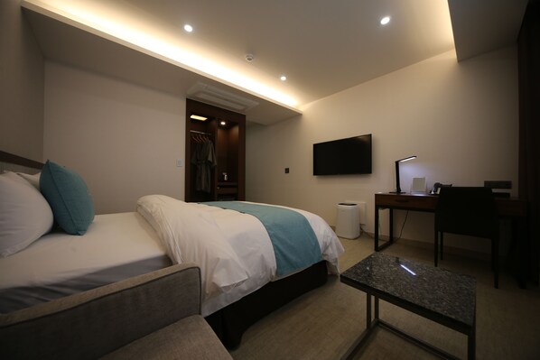 Habitación de hotel con cama, escritorio, silla, televisor y baño visible a través de una puerta abierta.