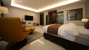 A modern hotel room with a large bed, a sofa, a TV, and a walk-in closet.