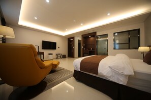 A modern hotel room with a large bed, a sofa, a TV, and a walk-in closet.