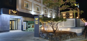 A hotel entrance with a sign indicating 'Grand Open' and a '7 Plus' sign above.