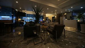 A modern hotel lobby with a marble floor, comfortable seating, a large plant, and a television screen.