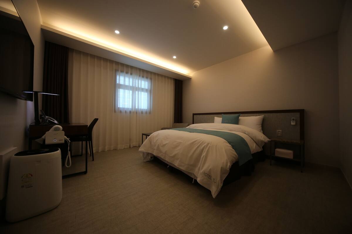 A hotel room with a large bed, a desk with a telephone, and a wall-mounted TV.