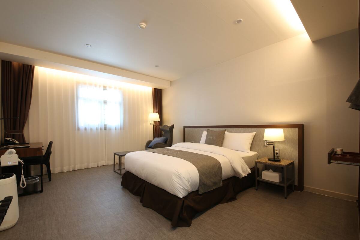 A hotel room with a large bed, bedside tables, a desk, and a chair.