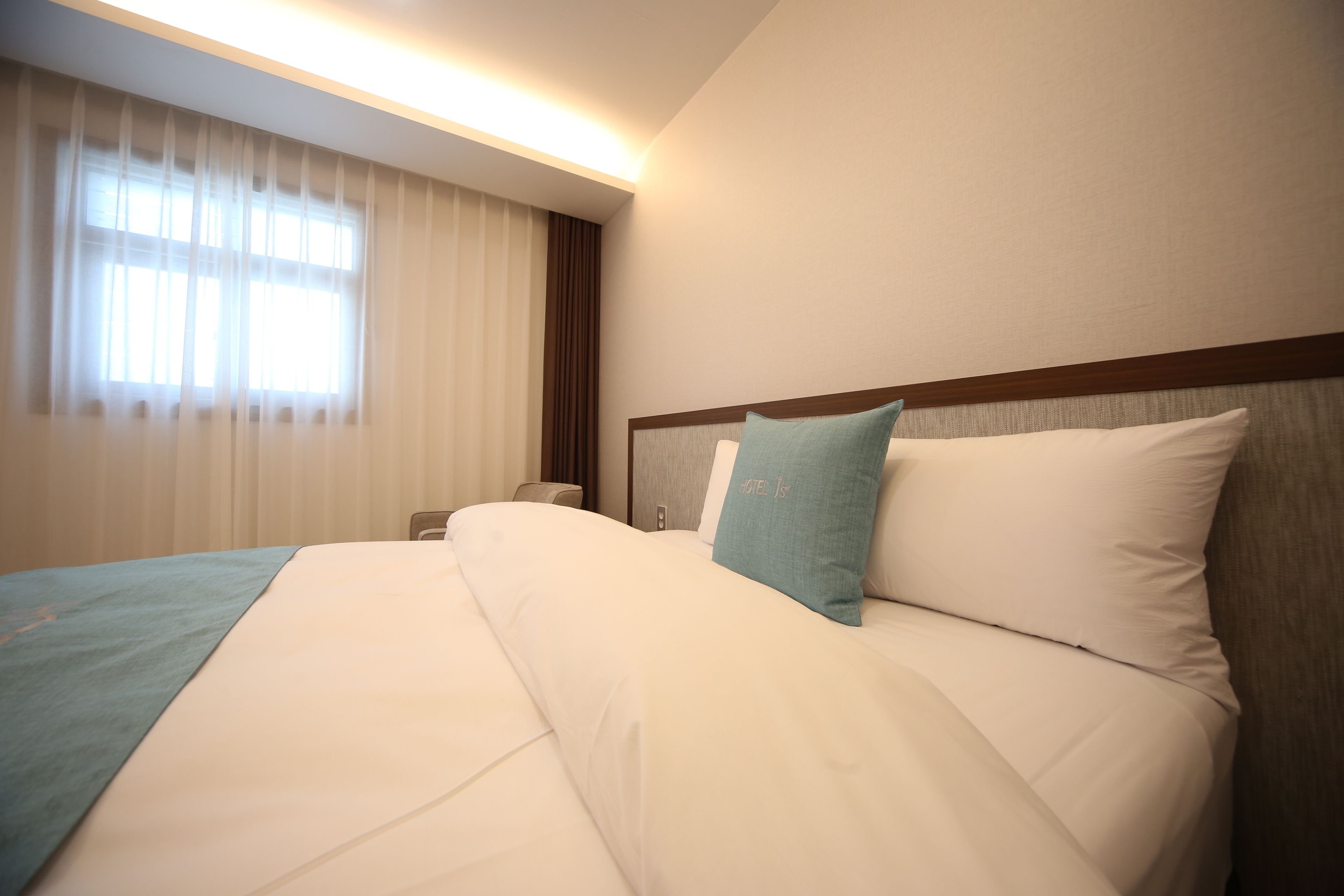 Habitación de hotel con una cama grande, una mesita de noche y un ventanal con cortinas.