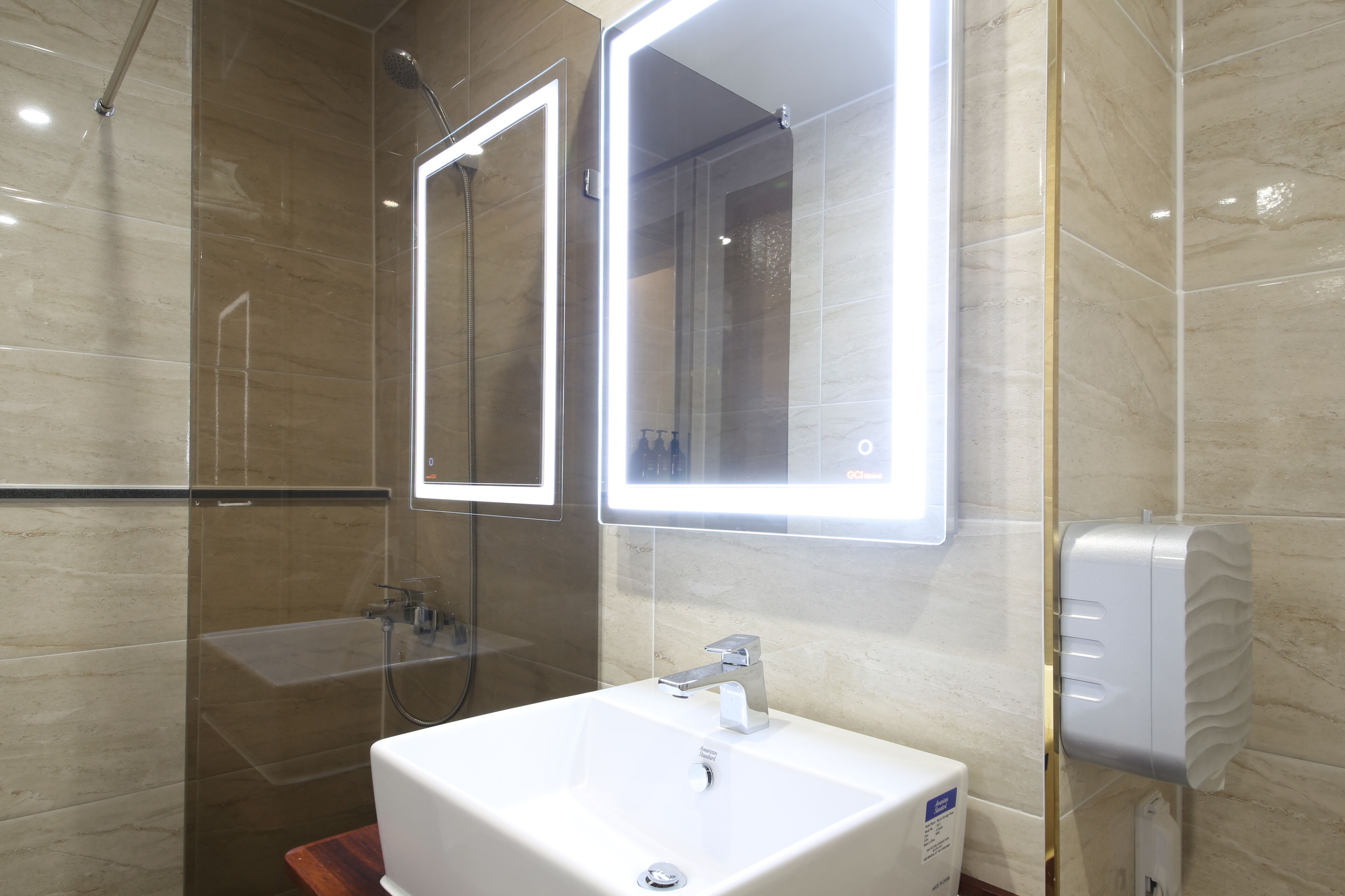 A modern bathroom with a glass-enclosed shower, a white sink, and a mirror with built-in lighting.