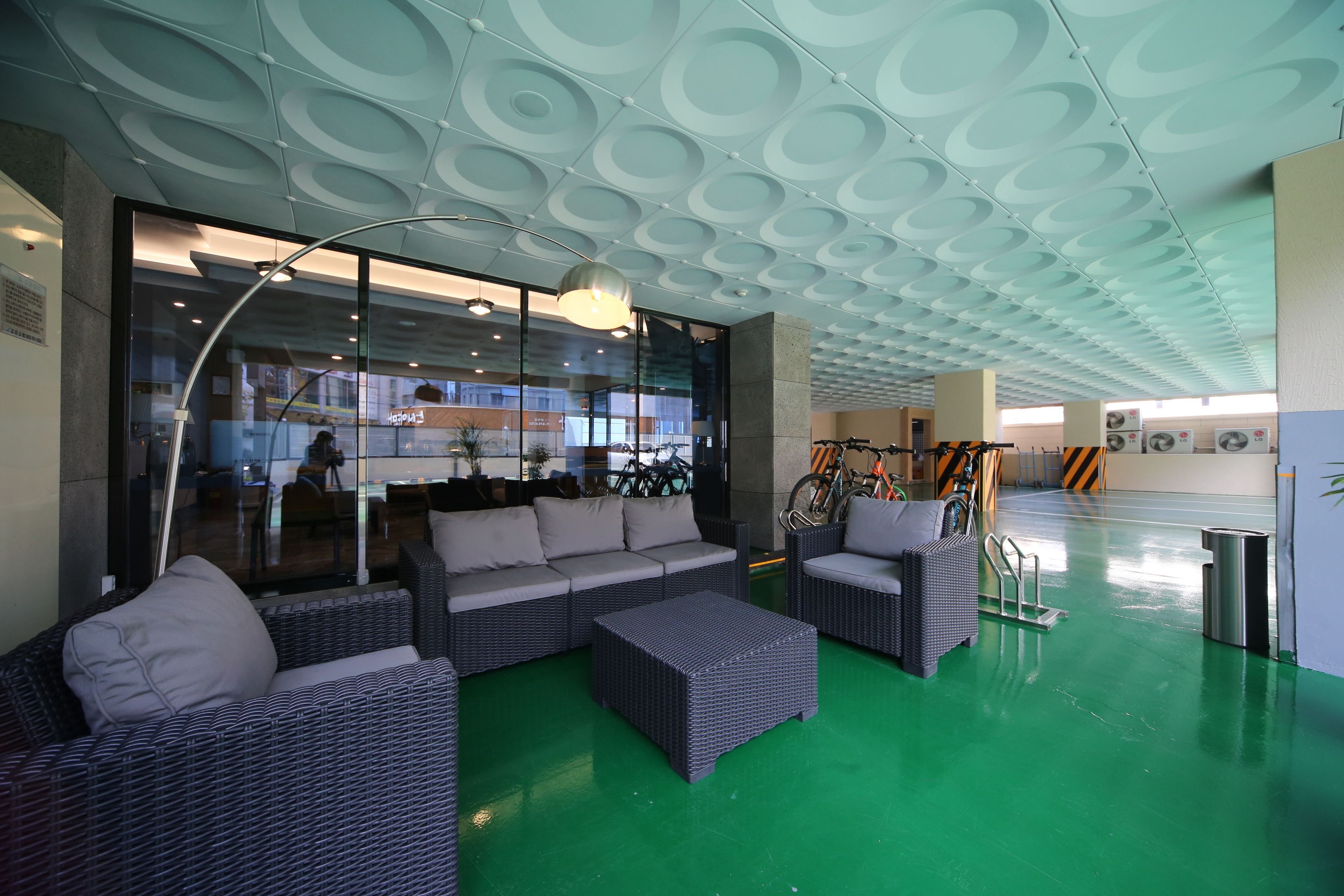 A modern lounge area with wicker furniture, a green floor, and a ceiling with circular patterns.