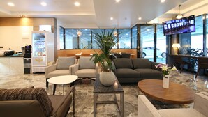 Una hall d'albergo moderna con zone relax, una macchina del caffè, un televisore e un'ampia finestra.