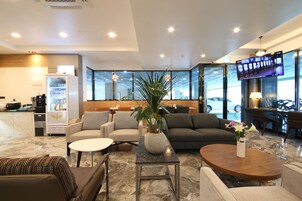 A modern hotel lobby with seating areas, a coffee machine, a TV, and a large window.