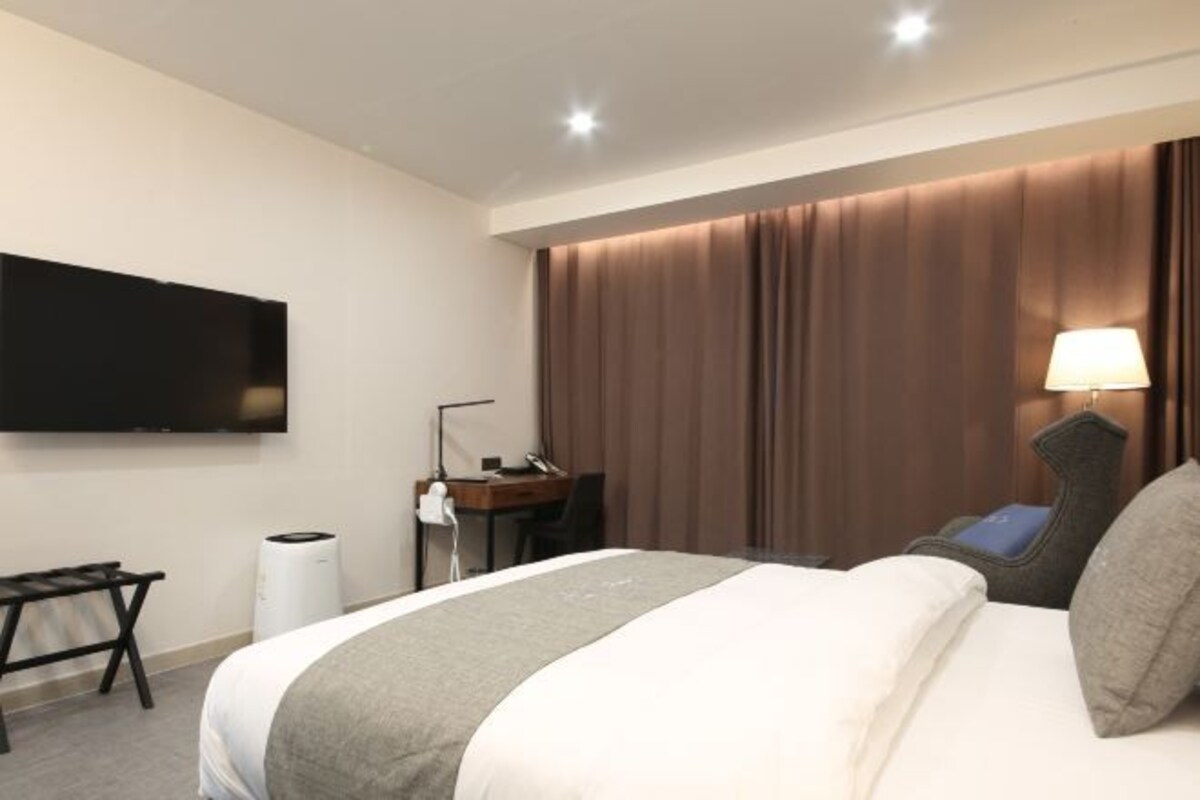 Habitación de hotel con cama, escritorio, silla, televisor y lámpara.