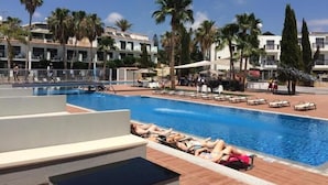 Zona de piscina con sillones de descanso y palmeras.