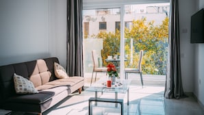 Una sala de estar moderna con un sofá, una mesa de centro de vidrio y vistas a un jardín lleno de flores amarillas.