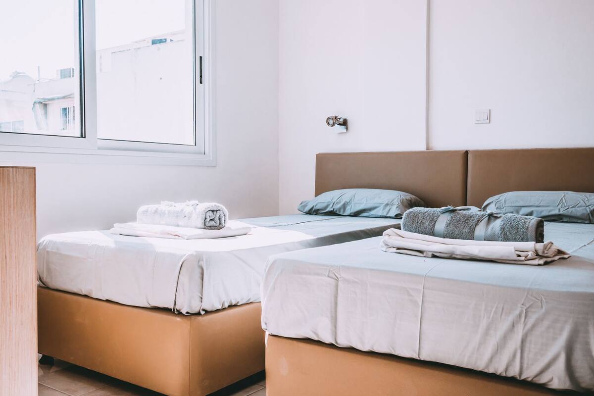 Une chambre d’hôtel avec deux lits, un bureau en bois et une fenêtre donnant sur des immeubles.
