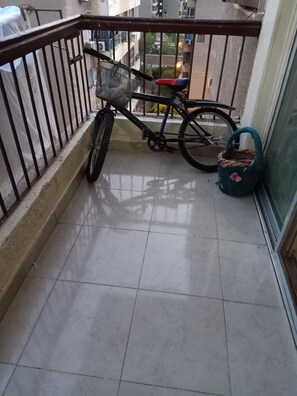 Ein Balkon mit einem Fahrrad, einem Korbwägelchen und einer blauen Tasche.