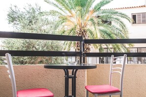 A balcony with two white chairs and a small round table, surrounded by a textured wall and palm trees. - Pan Marie Apartments (Ayia Napa)