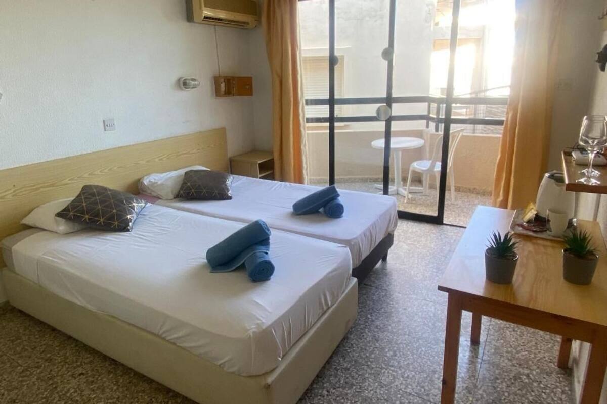 Une chambre d’hôtel avec deux lits, une petite table avec une plante et un balcon avec une table et des chaises.