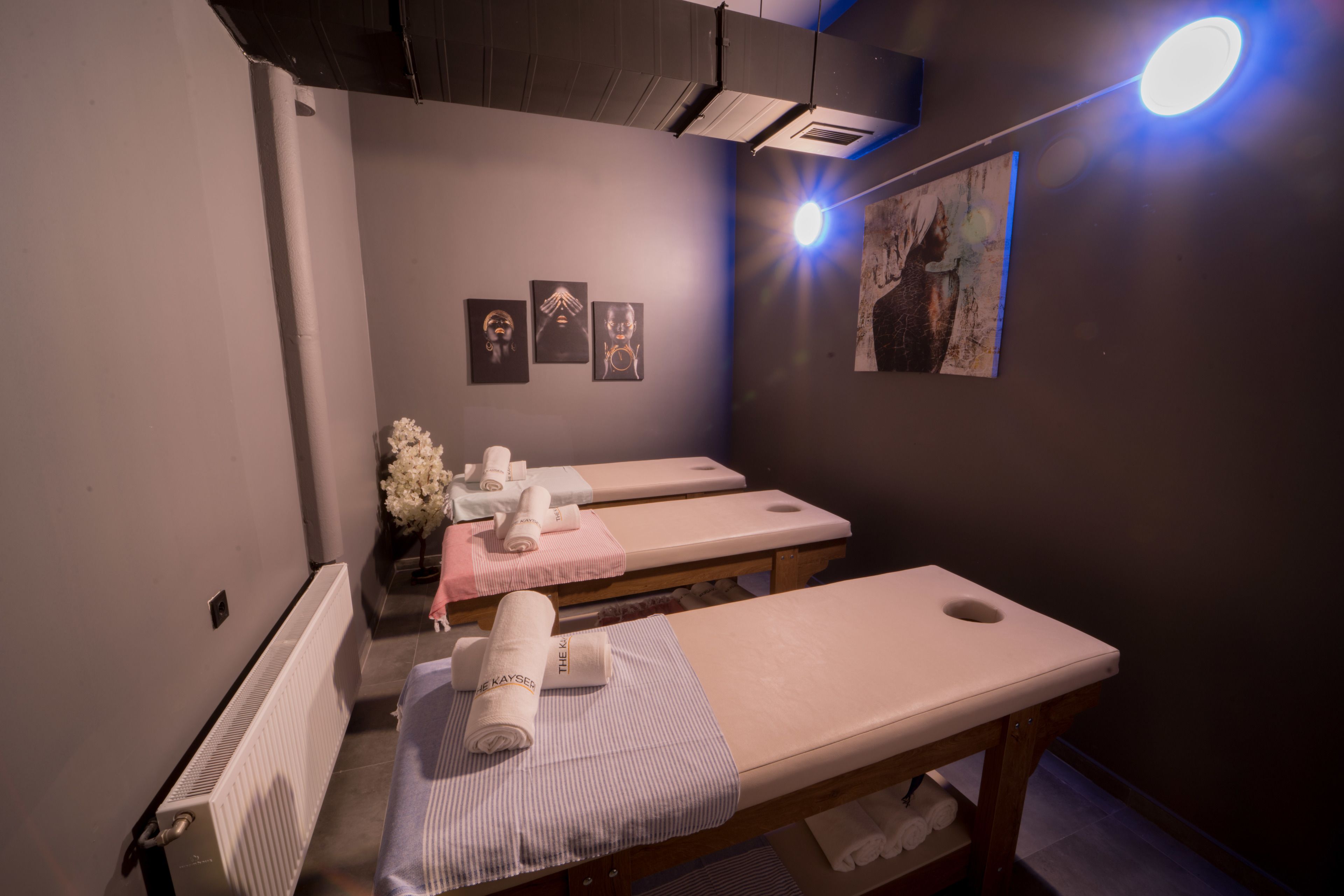 Um salão de spa com três mesas de tratamento, um radiador e obras de arte nas paredes.