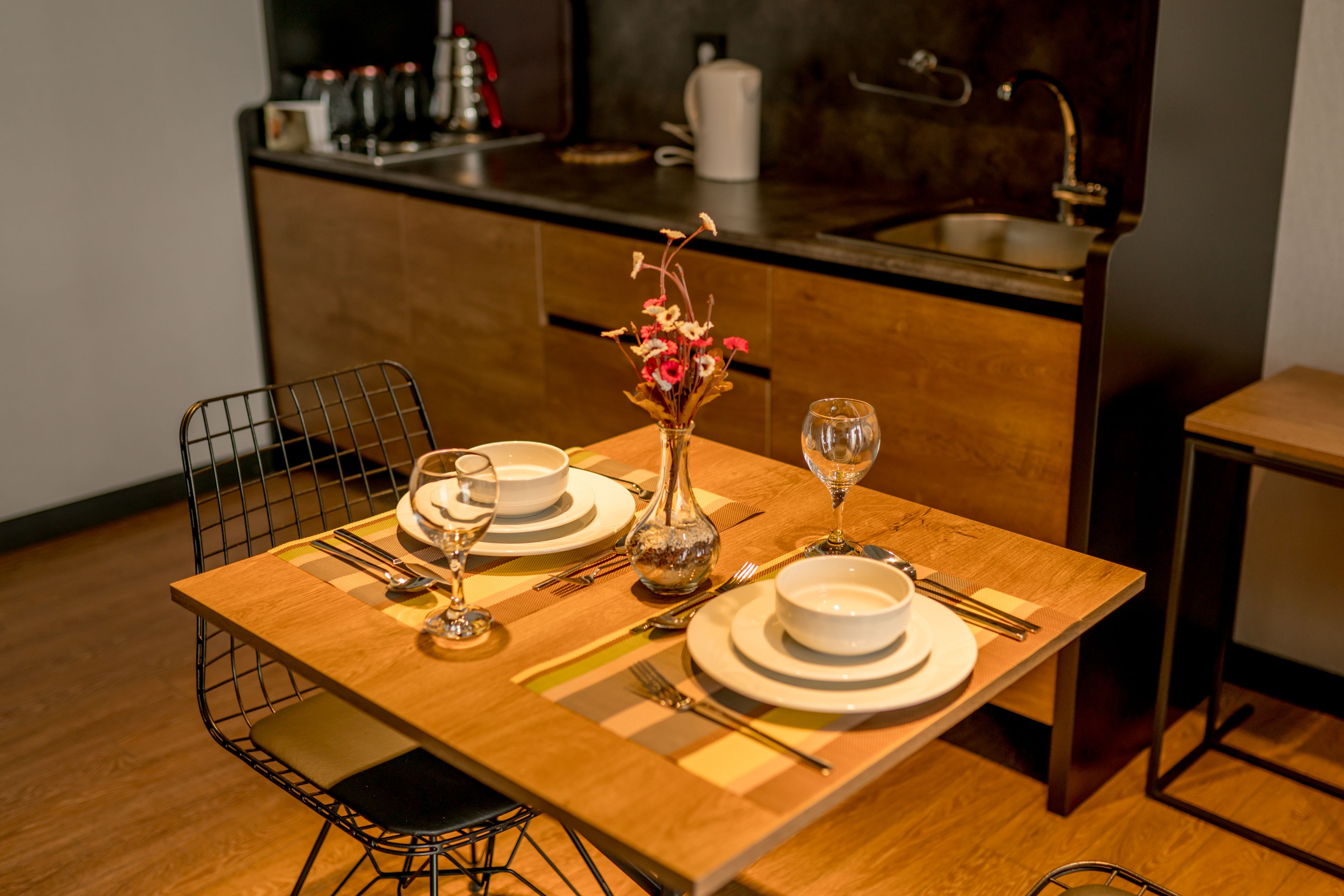 A dining table set with plates, bowls, cutlery, and a vase with flowers.