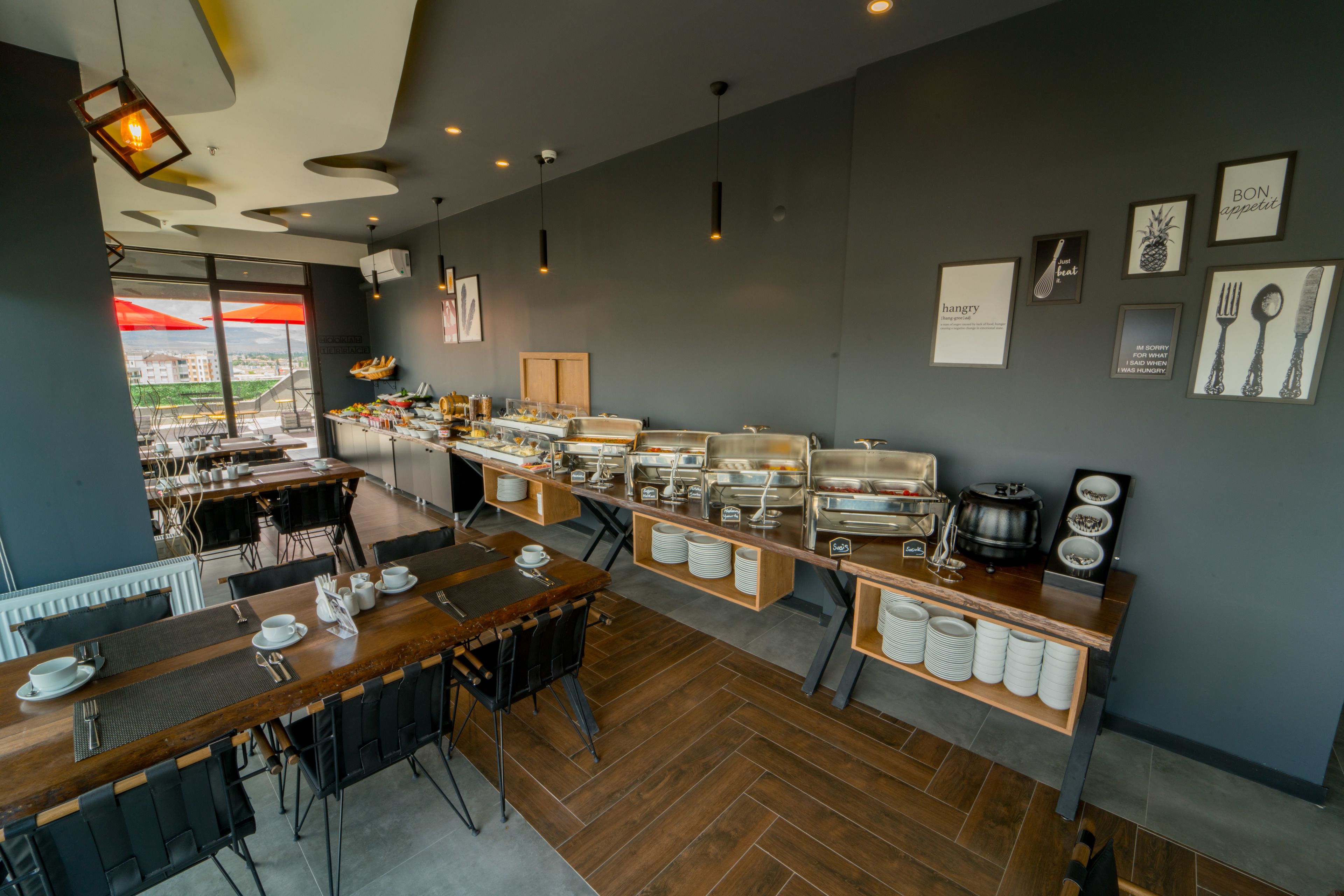 Un desayuno buffet moderno con diversas opciones de comida, una zona de estar con mesas y sillas, y vistas al exterior a través de amplias ventanas.
