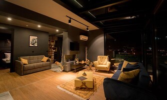 A modern living room with a sofa, armchair, and coffee table, a bookshelf, and a TV.