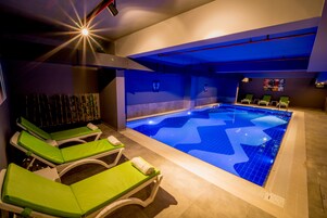 A swimming pool with blue tiles, green lounge chairs, and a ceiling light.
