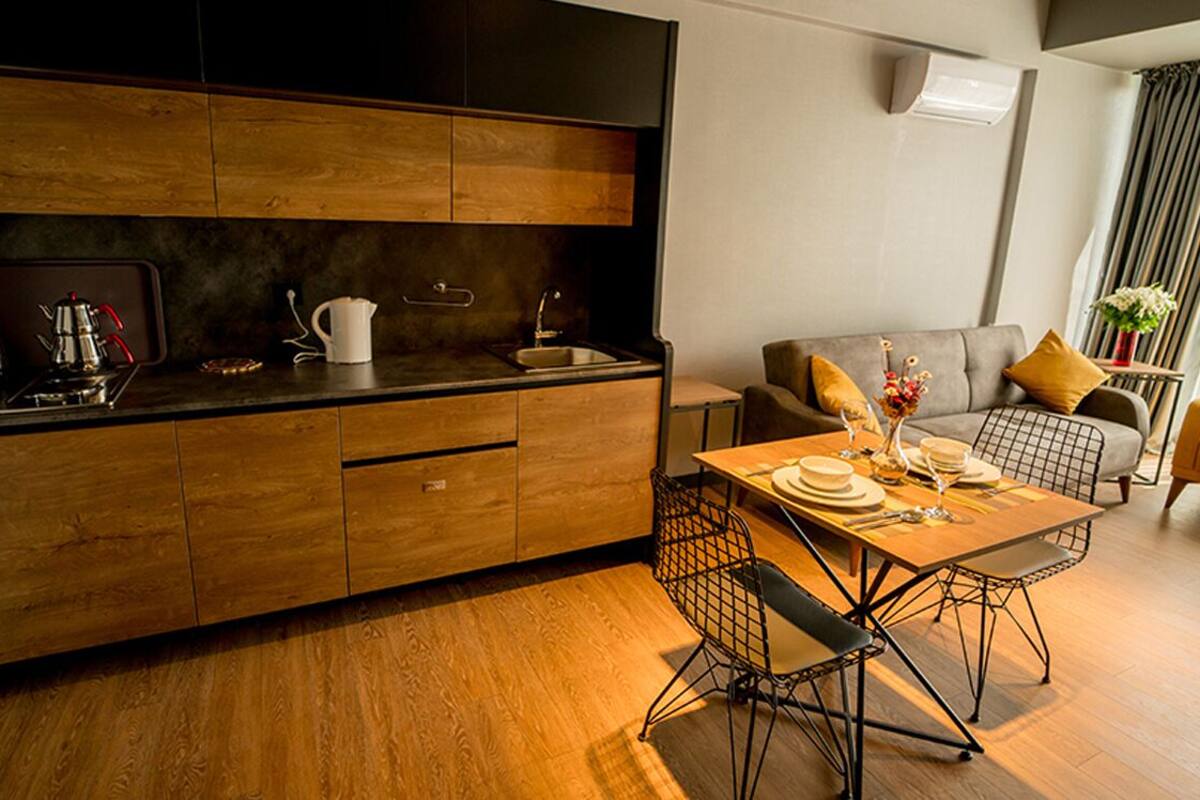 Eine moderne Küche mit Holzausbau, einem Esstisch mit Metallstühlen und einem grauen Sofa im angrenzenden Wohnbereich.